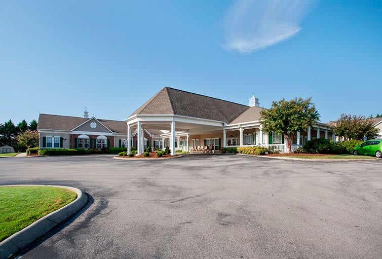 A spacious building with a large entrance and circular driveway under a clear blue sky.