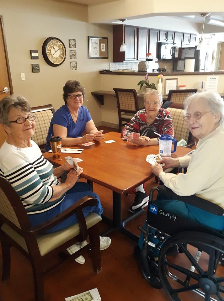 A group of senior women socializing and playing a card game indoors.