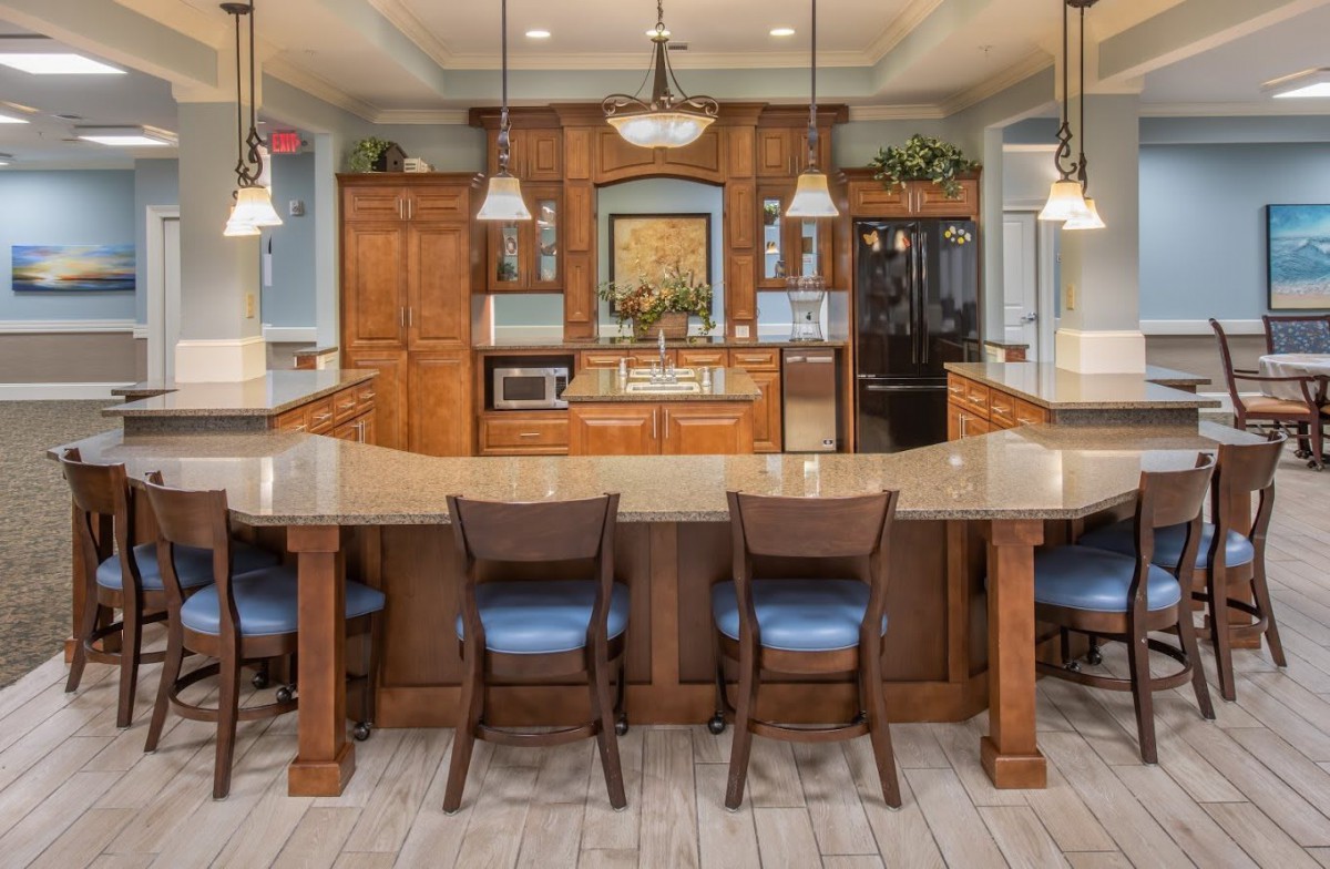 A spacious kitchen with wooden cabinetry, modern pendant lighting, and a large central countertop with bar stools.