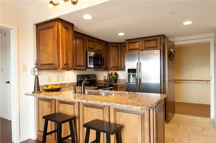 A modern kitchen with wooden cabinets, a granite countertop island, and stainless steel appliances.