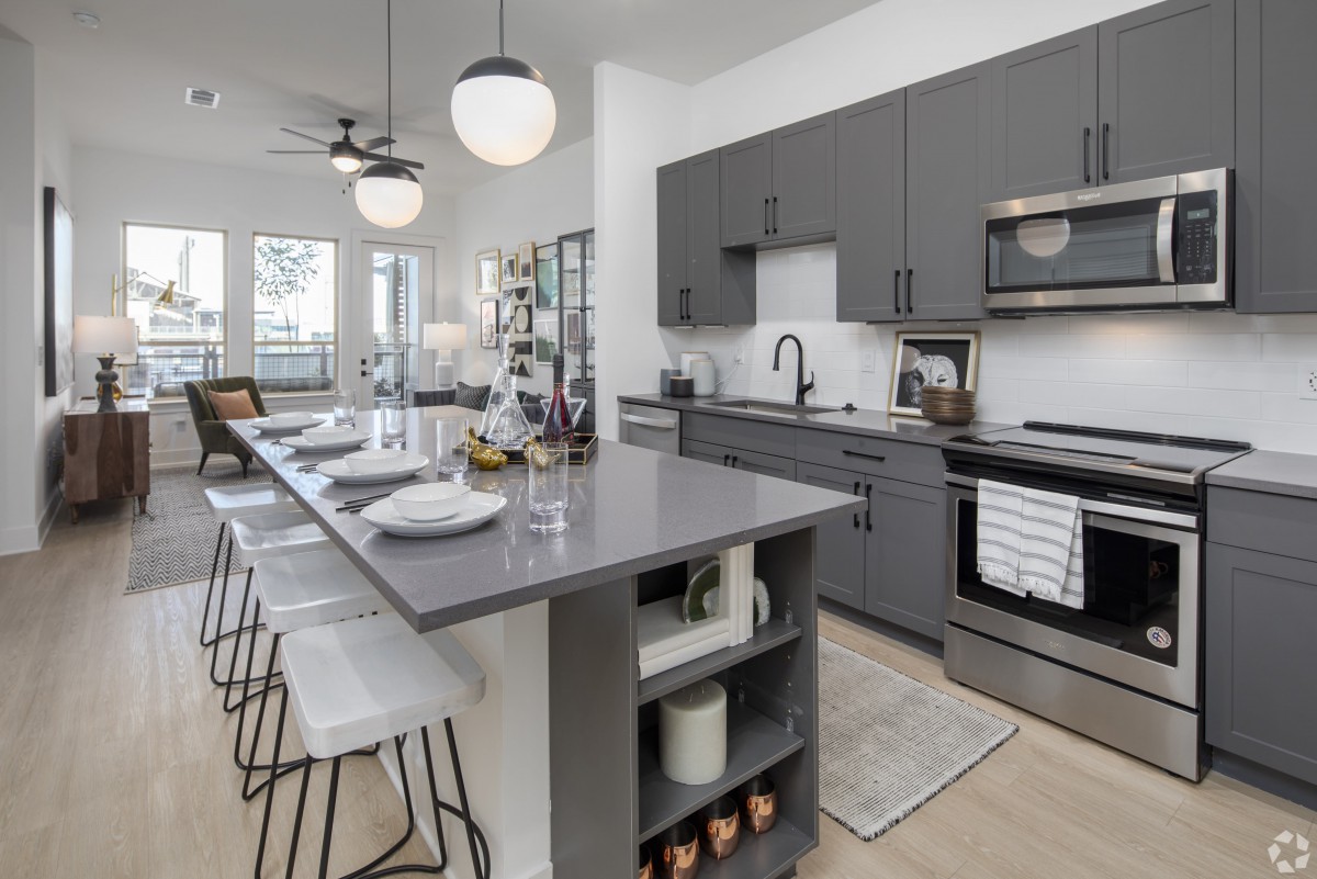 A modern kitchen with gray cabinets and an island counter equipped with bar stools and pendant lighting.