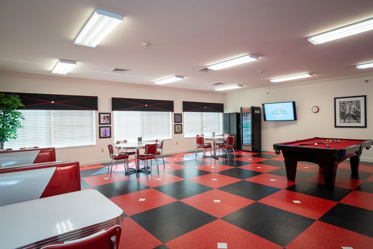 A spacious break room featuring a checkered red and black floor, with multiple tables and chairs, a pool table, vending machine, and television.