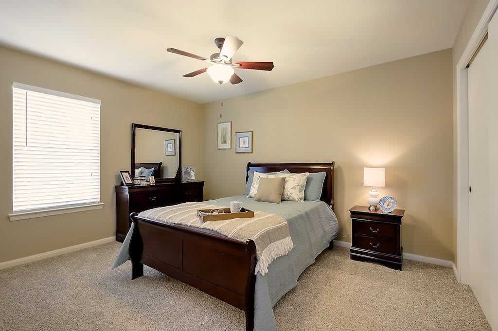 A cozy bedroom with a well-made bed, nightstand, and mirror in a warmly lit interior.