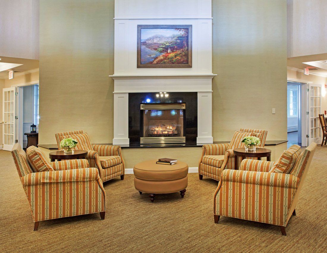 A cozy living room with armchairs arranged around a fireplace, adorned with a painting above.