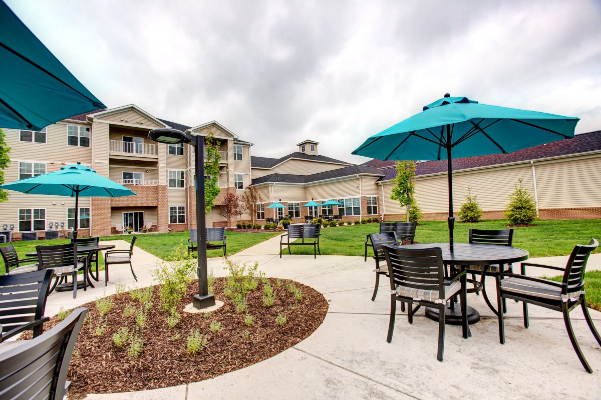 A spacious outdoor patio area with tables, chairs, and umbrellas in front of a building on a cloudy day.