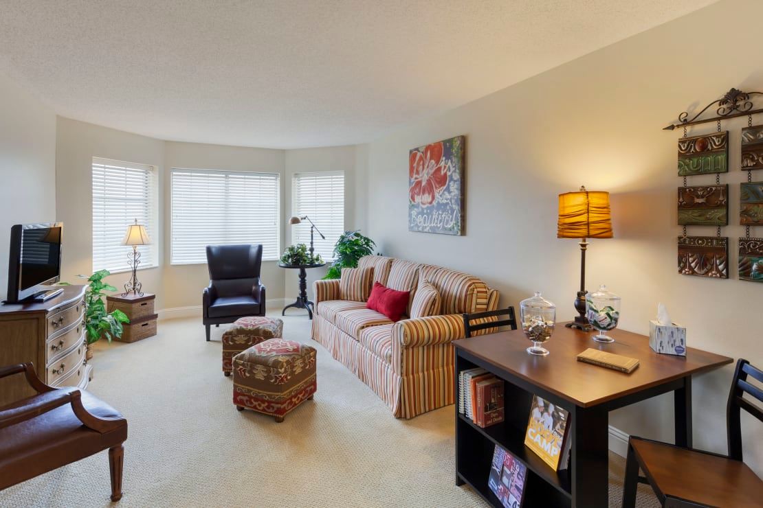 A cozy living room with a sofa, armchair, and a desk, warmly lit by lamps.