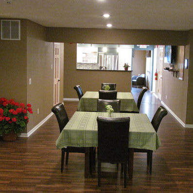A cozy dining area with tables and chairs, featuring green tablecloths and wood flooring.