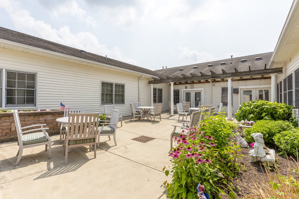 A bright courtyard featuring outdoor furniture, a pergola, and colorful flowers.