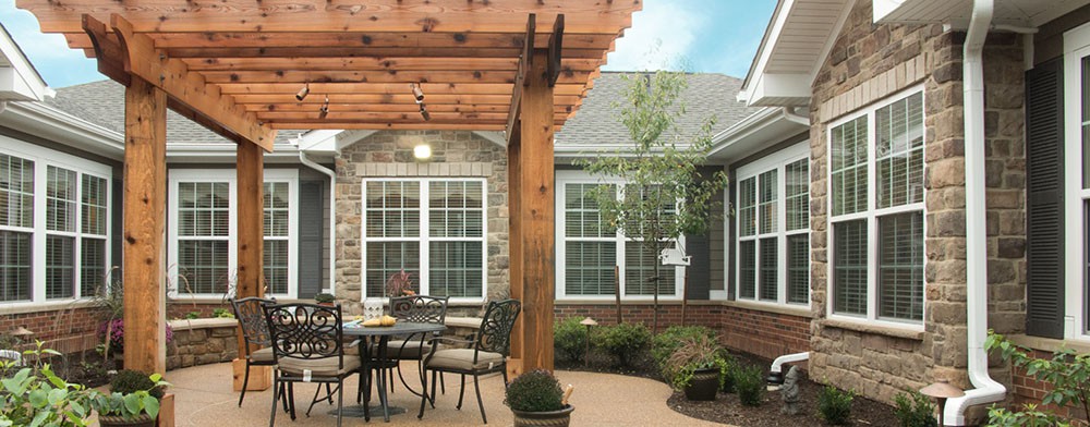 A cozy patio with a wooden pergola, featuring outdoor furniture and potted plants.