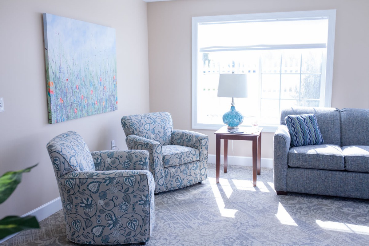 A bright and cozy living room with patterned chairs, a sofa, and a lamp by the window.