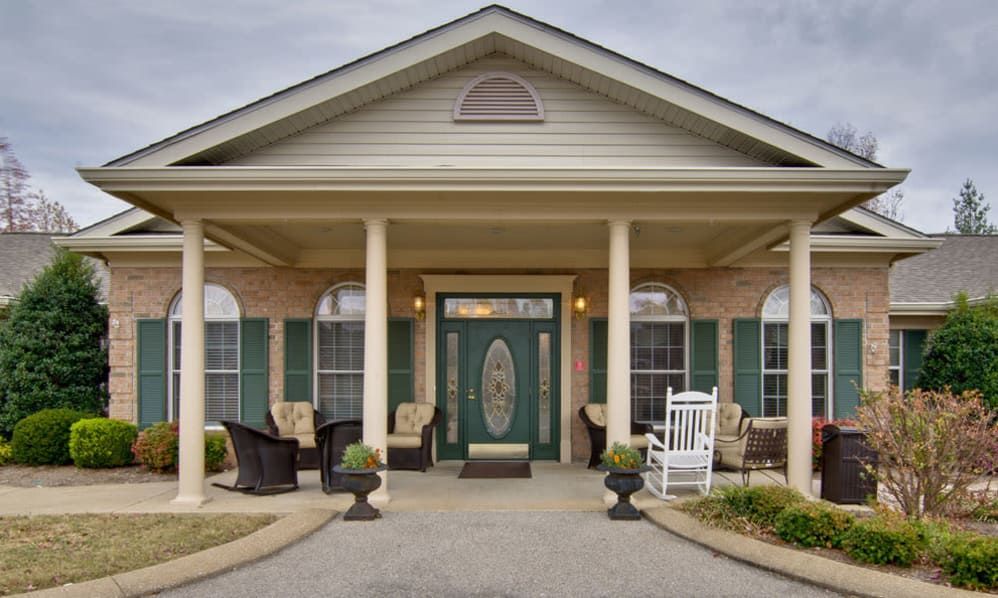 A charming front porch with columns, rocking chair, and potted plants leading to a residential entrance.