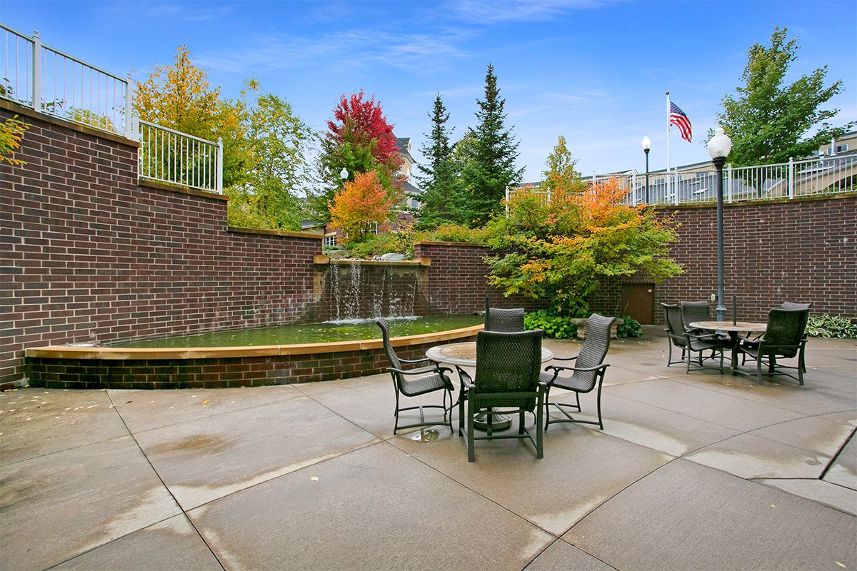 A serene outdoor patio area featuring a fountain, surrounded by fall foliage and equipped with tables and chairs for seating.