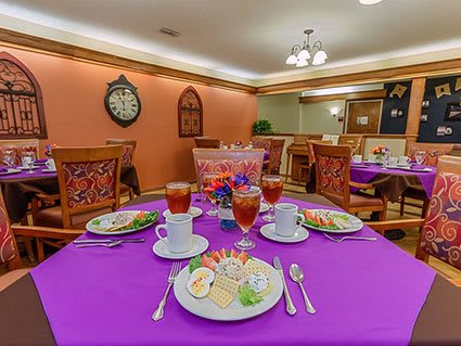 A cozy dining room with elegantly set tables, featuring a purple tablecloth and fine dinnerware.