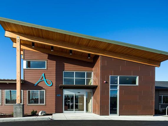 A modern building with a sloped roof and wood exterior, featuring large windows and a main entrance.