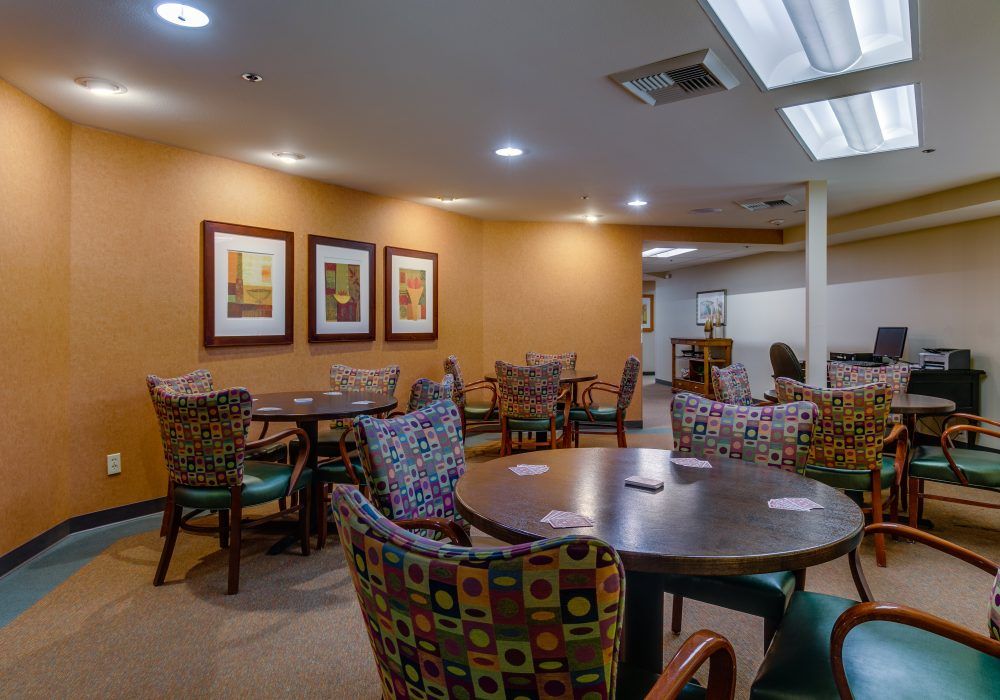 A cozy dining area with multiple tables and colorful chairs, decorated with framed artwork on the walls.