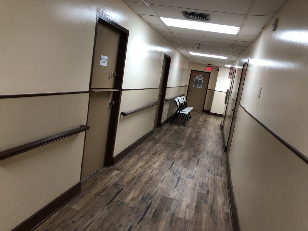 A dimly lit hospital hallway with doors on either side and seating at the end.
