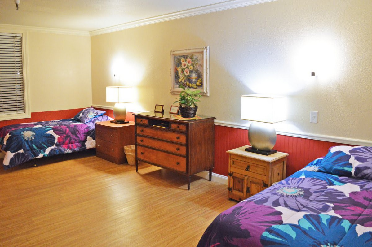 A cozy bedroom featuring twin beds with floral bedding, illuminated by table lamps on wooden nightstands against a warm-toned wall.