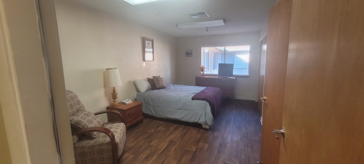 A cozy bedroom with a bed, nightstand, lamp, and a window letting in natural light.