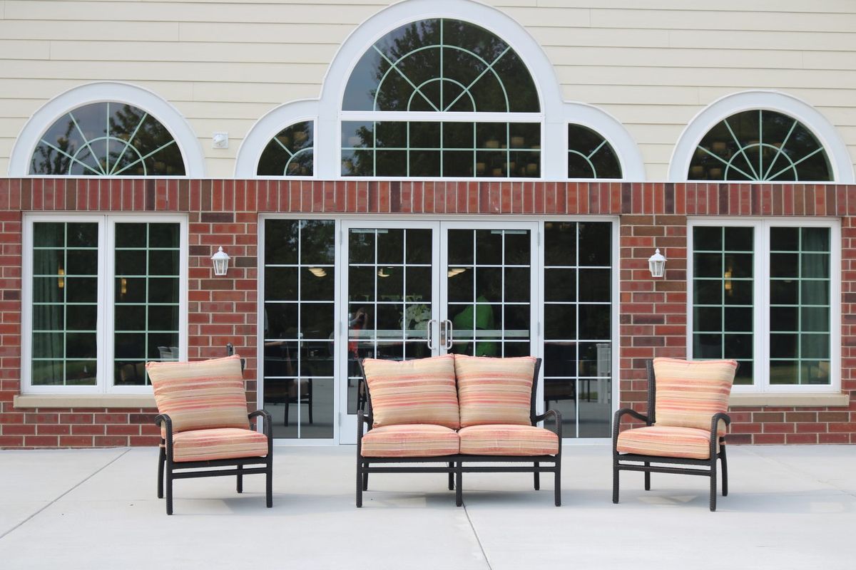 Outdoor patio area with cushioned furniture in front of large windows and a brick wall.