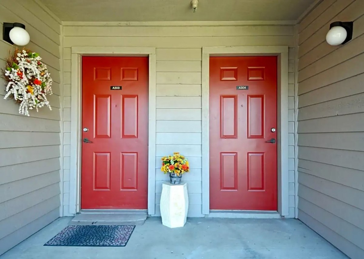 Two red apartment doors with a vase of flowers in between.