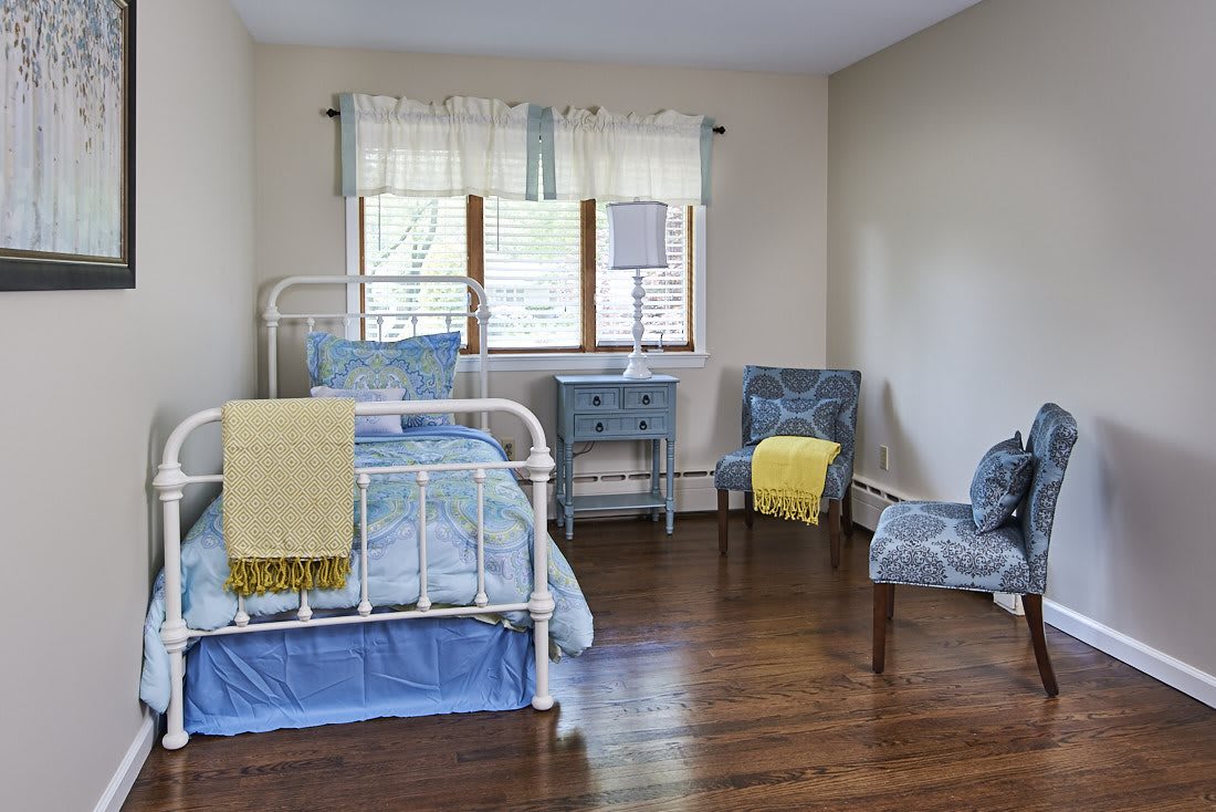 A cozy bedroom with a metal framed bed, blue accents, and wooden flooring.