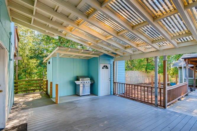 A covered outdoor patio with a grill and fenced backyard.