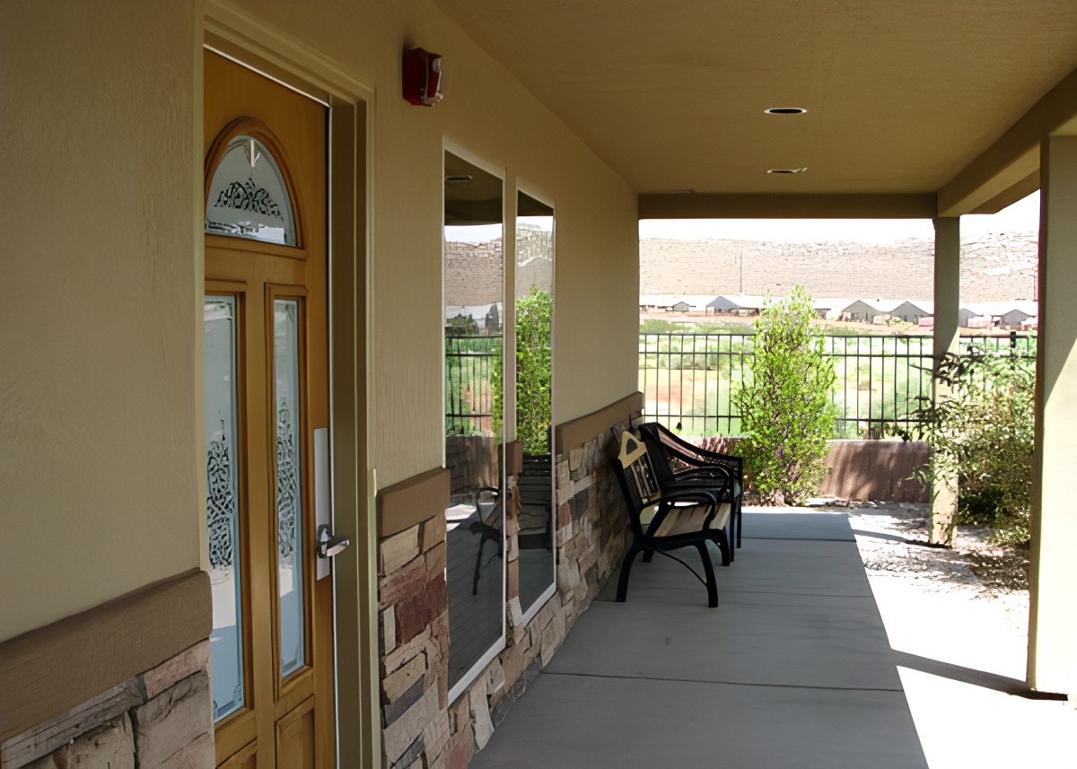 A sunny porch with a bench, door, and windows overlooking a fenced area.