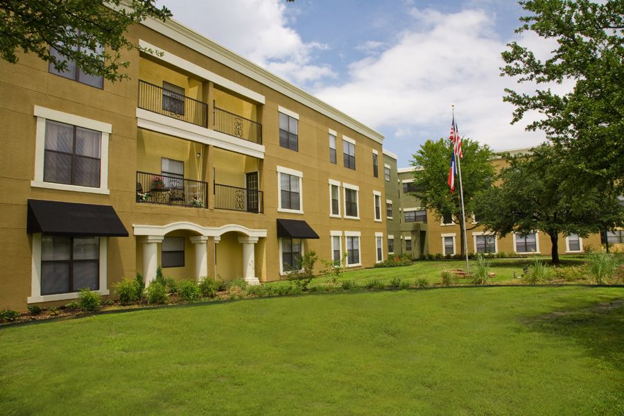 A three-story apartment building with a well-maintained lawn and balconies.