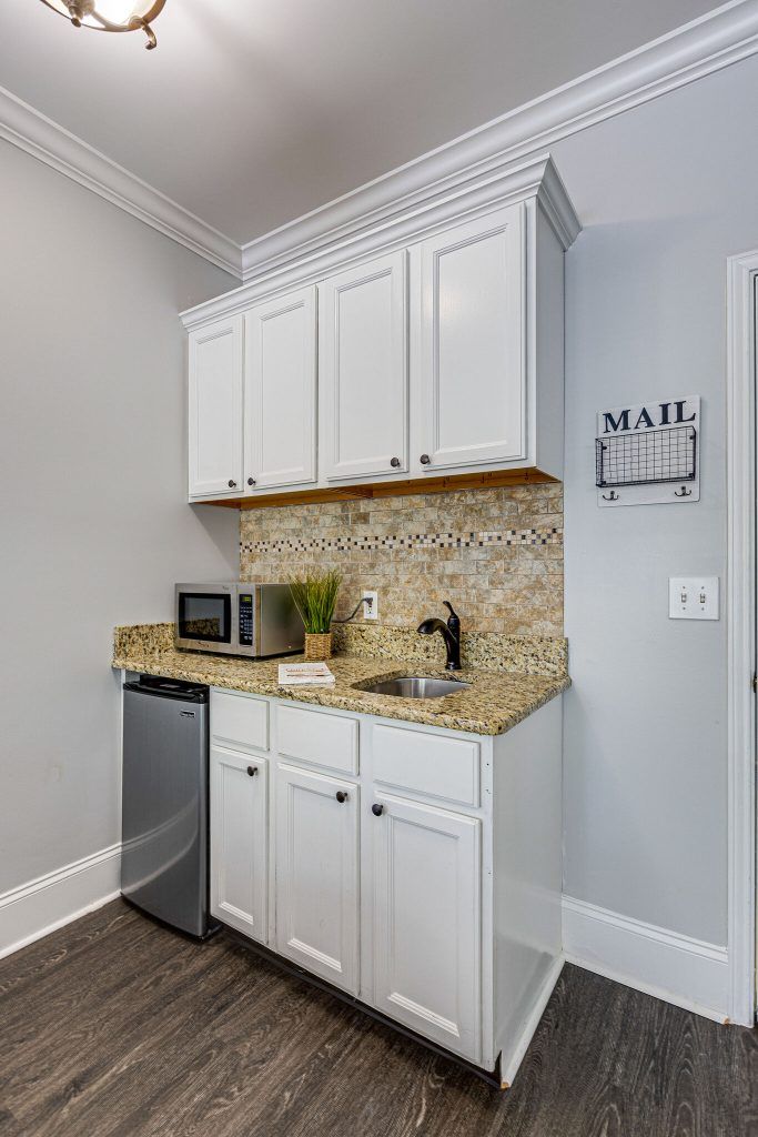 A compact kitchenette featuring a mini fridge, microwave, sink, and white cabinetry.