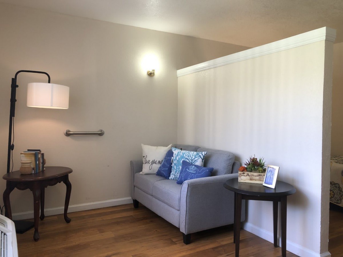 A cozy living room with a small sofa and decorative pillows, illuminated by a wall-mounted lamp.