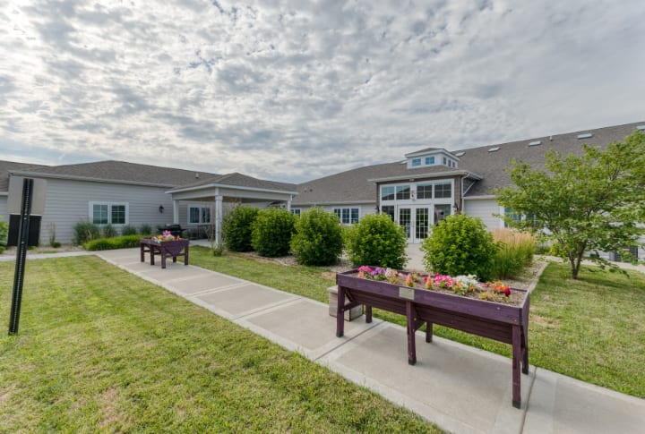 A landscaped area with benches and a pathway in front of a building under a cloudy sky.
