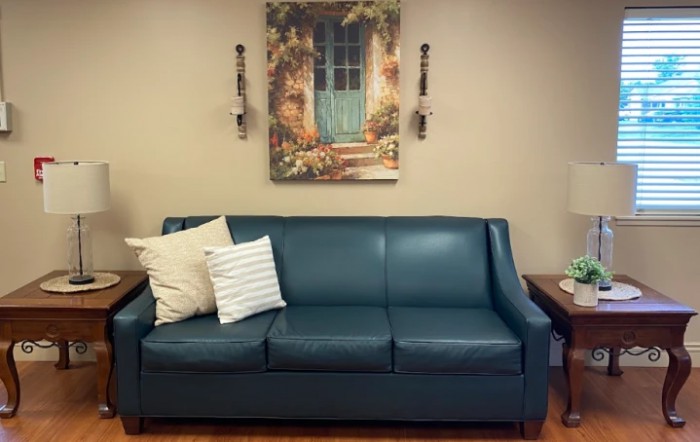 A cozy living room setup featuring a teal sofa with decorative pillows and a scenic painting above.