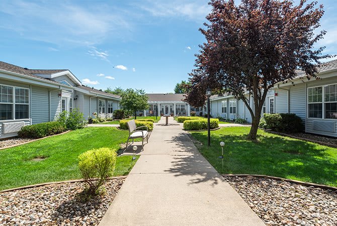 A landscaped garden with a pathway leading to a building, surrounded by trees and benches.