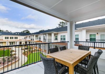 A spacious balcony with a wooden table and chairs overlooking a neatly landscaped residential complex.