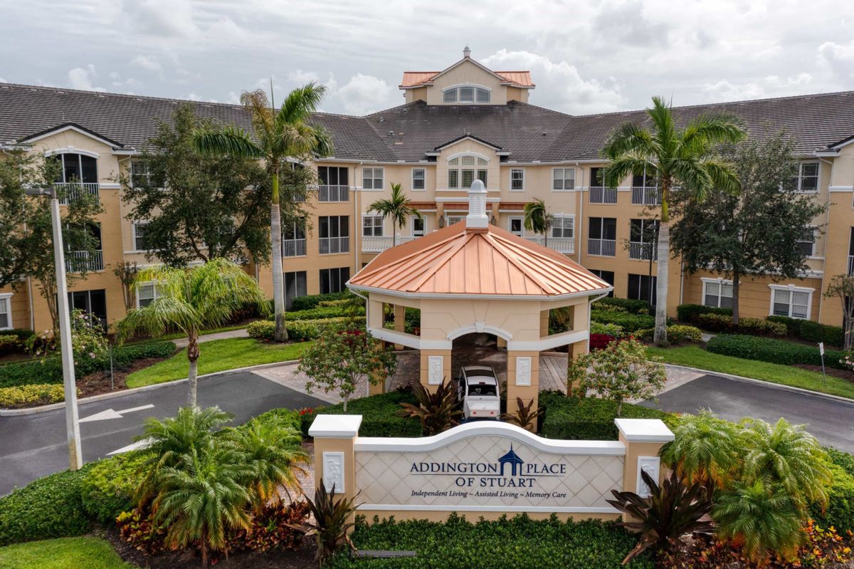 A scenic view of an elegant building surrounded by lush landscaping and palm trees, featuring a prominent entrance and sign.