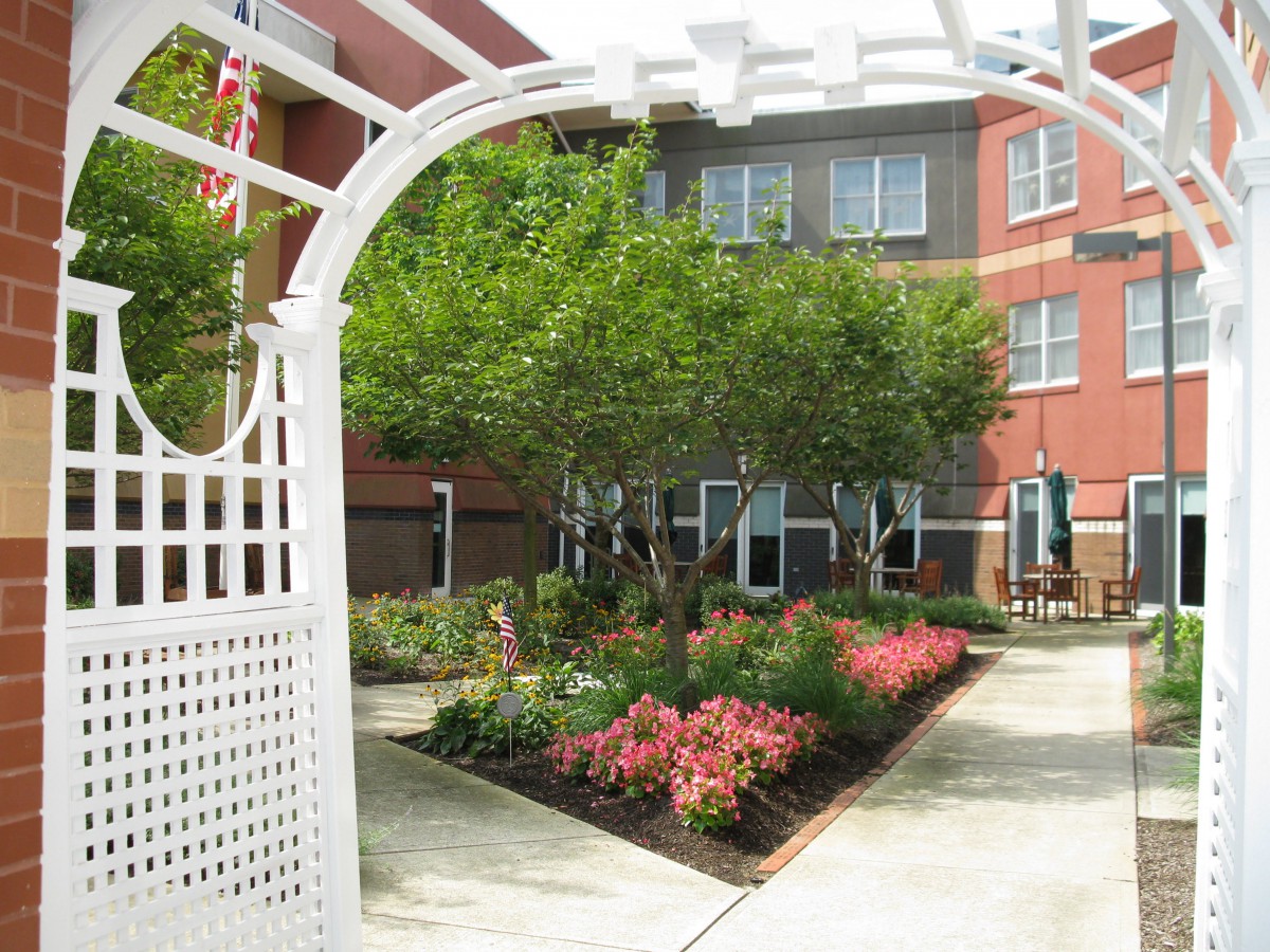 A beautiful courtyard garden with flowers and an archway in front of a brick building.