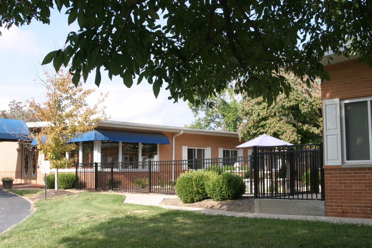 A small residential building with a blue awning, surrounded by trees and a fenced area.