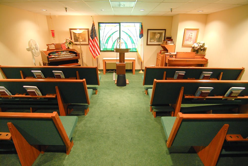 Interior view of a small chapel with rows of seating, podium, and flags.