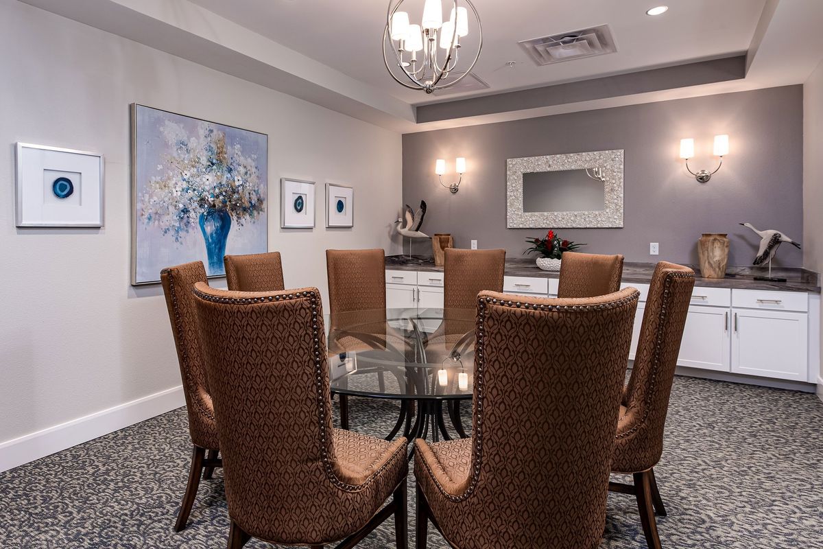 A well-decorated dining room with a glass table, brown chairs, a chandelier, and wall decor.