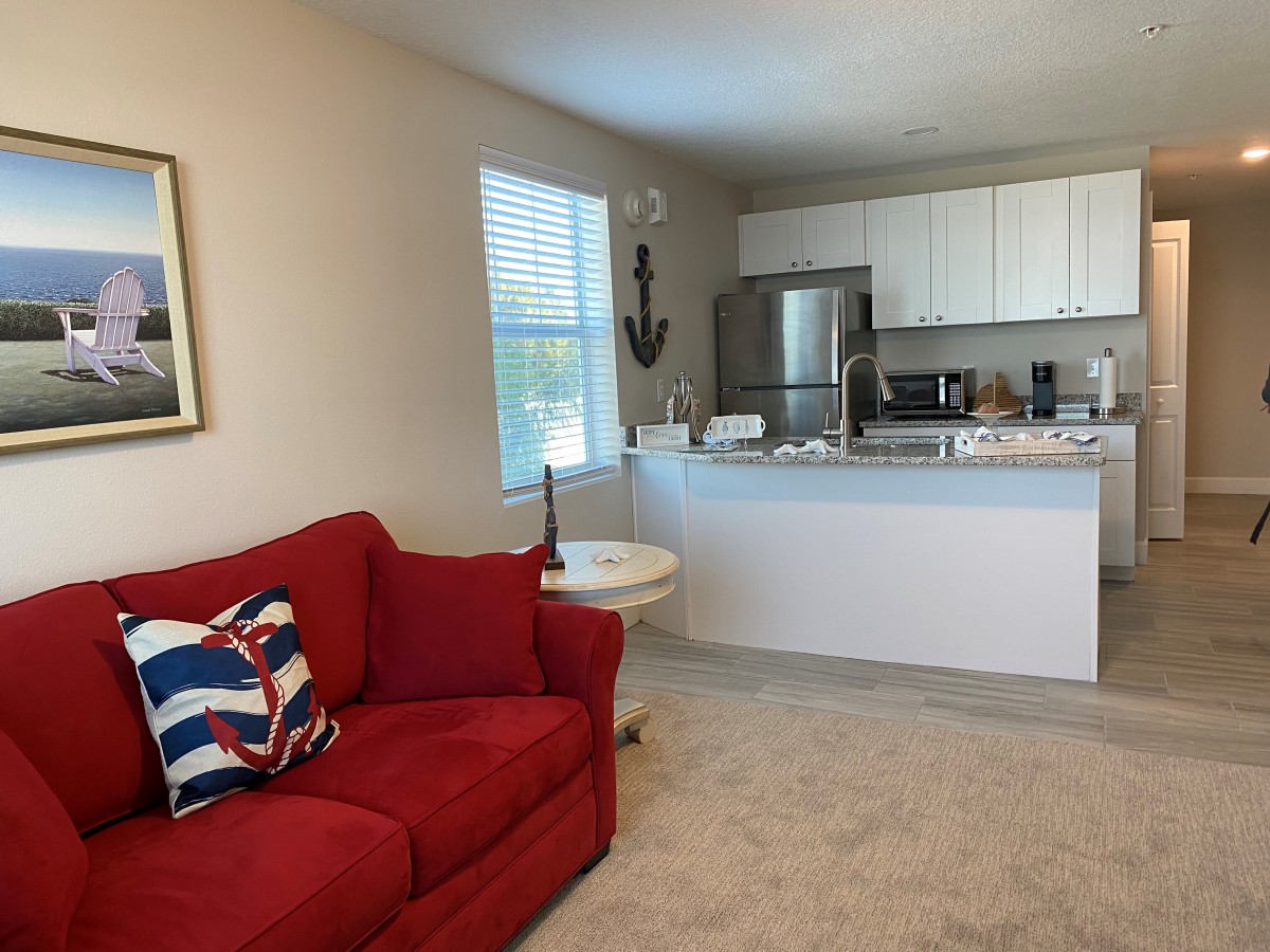An open concept living room with a red couch and adjacent kitchen area.
