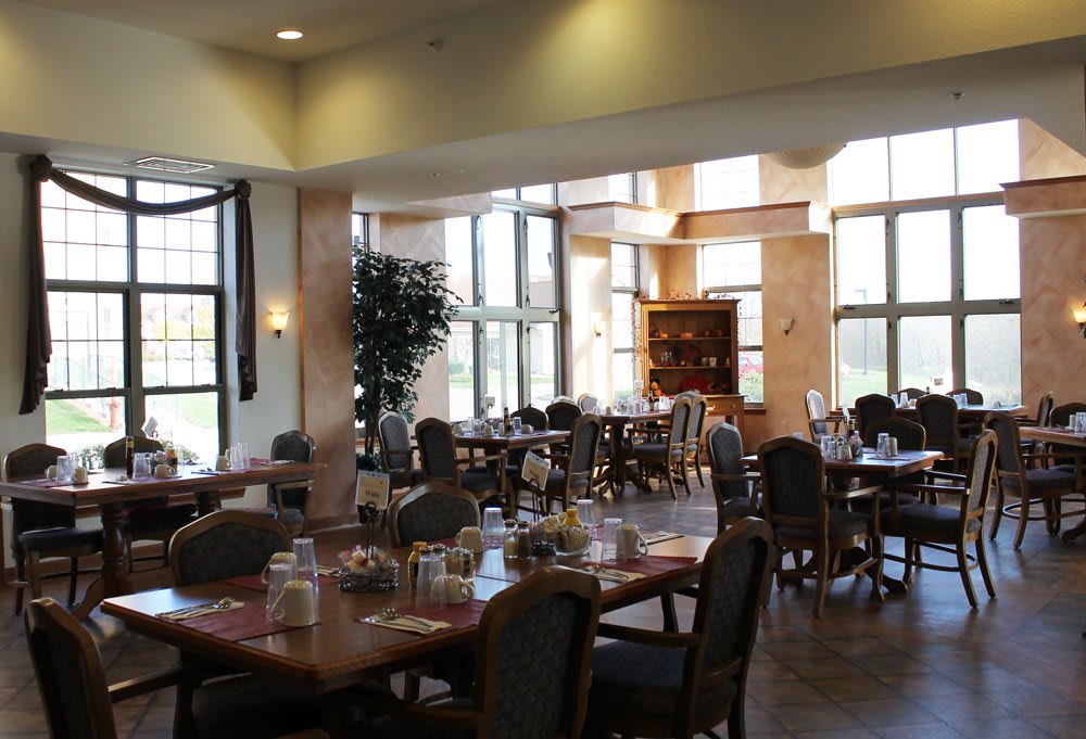 A spacious dining area with several tables and chairs, elegantly decorated and well-lit by large windows.