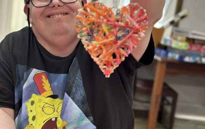 A person happily displaying a colorful string art heart.
