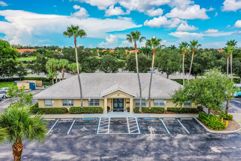 A building surrounded by palm trees with an empty parking lot on a partly cloudy day.