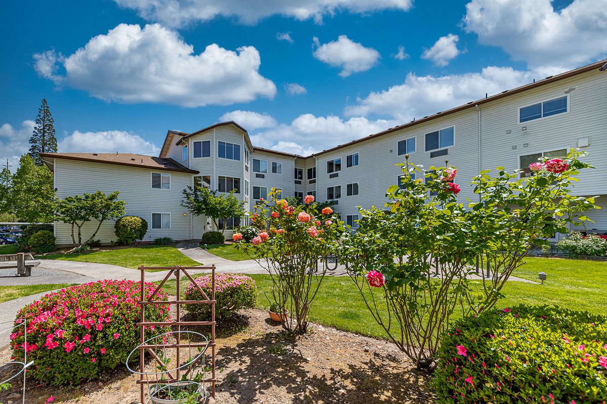 A residential building with well-maintained gardens and flowers under a partly cloudy sky.