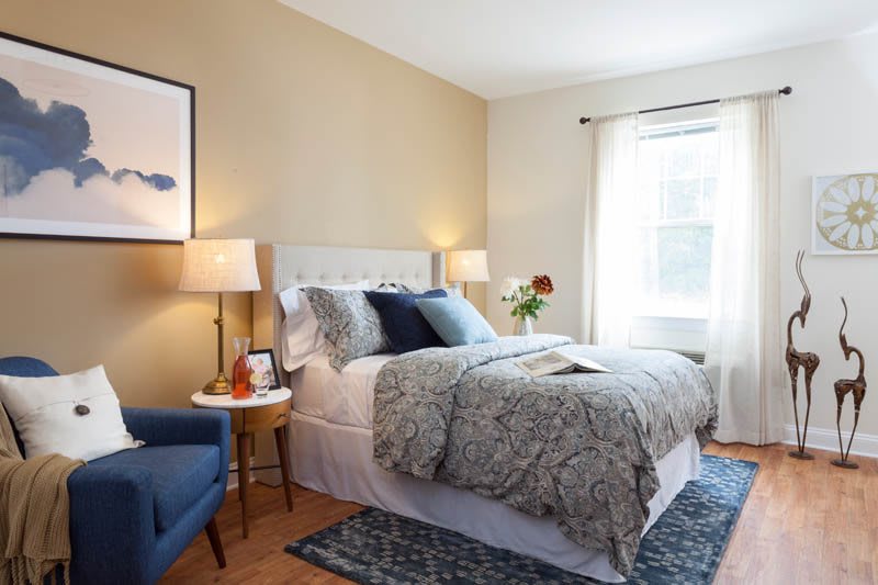 A cozy bedroom with a neatly made bed, two bedside lamps, and a comfortable chair by the window.