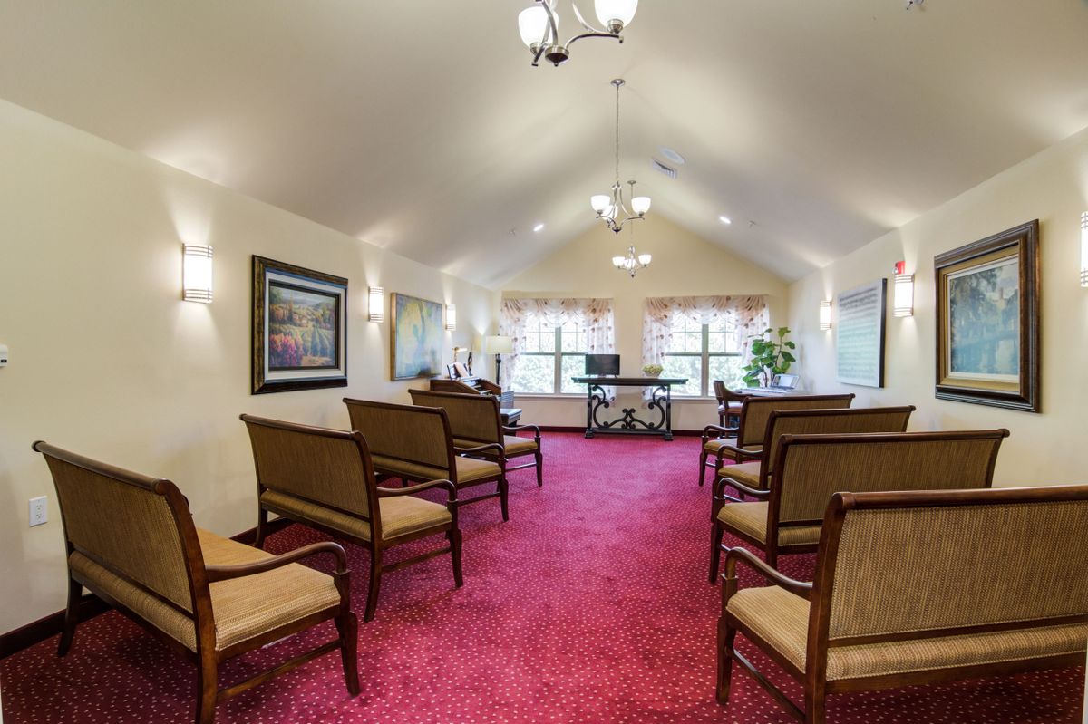A well-lit room with rows of chairs arranged on a vibrant red carpet, featuring large windows and decorative elements.