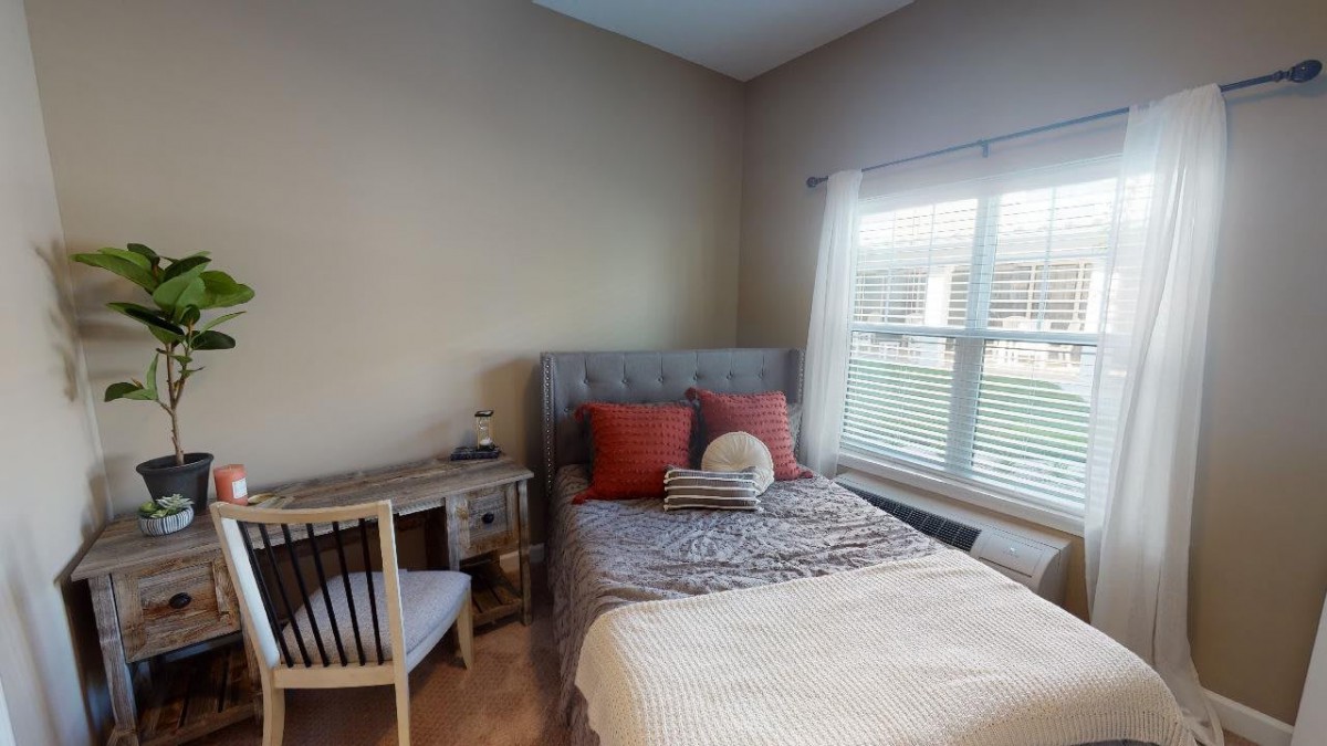 Cozy bedroom with a neatly made bed, a small desk and chair by the window.