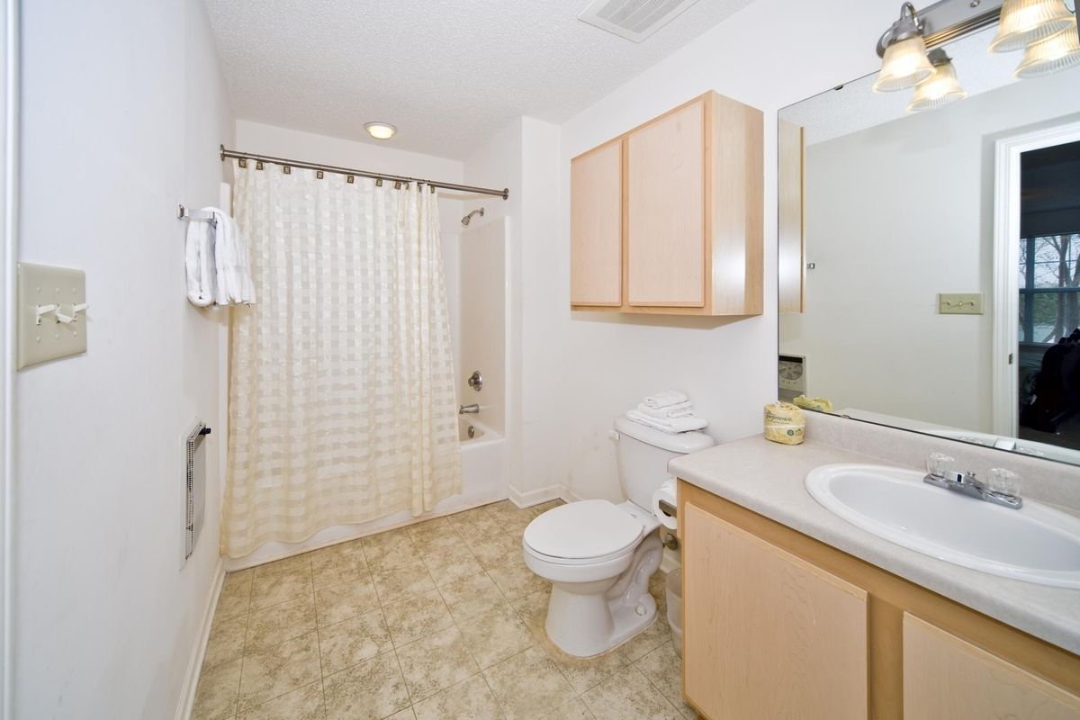 A clean and organized bathroom with a shower curtain, toilet, sink, mirror, and cabinet.