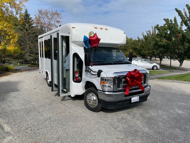 A white shuttle bus adorned with balloons and a large red ribbon parked outdoors.