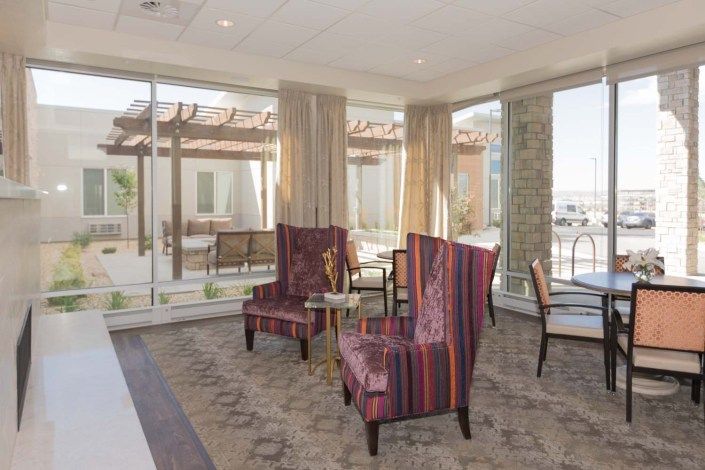 A bright and comfortable lobby with large windows, featuring colorful chairs and a view of the outdoor patio.